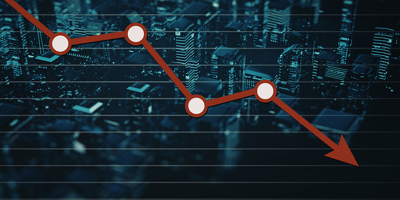 Red, graph line descending from top left to bottom right against a backdrop of a cityscape